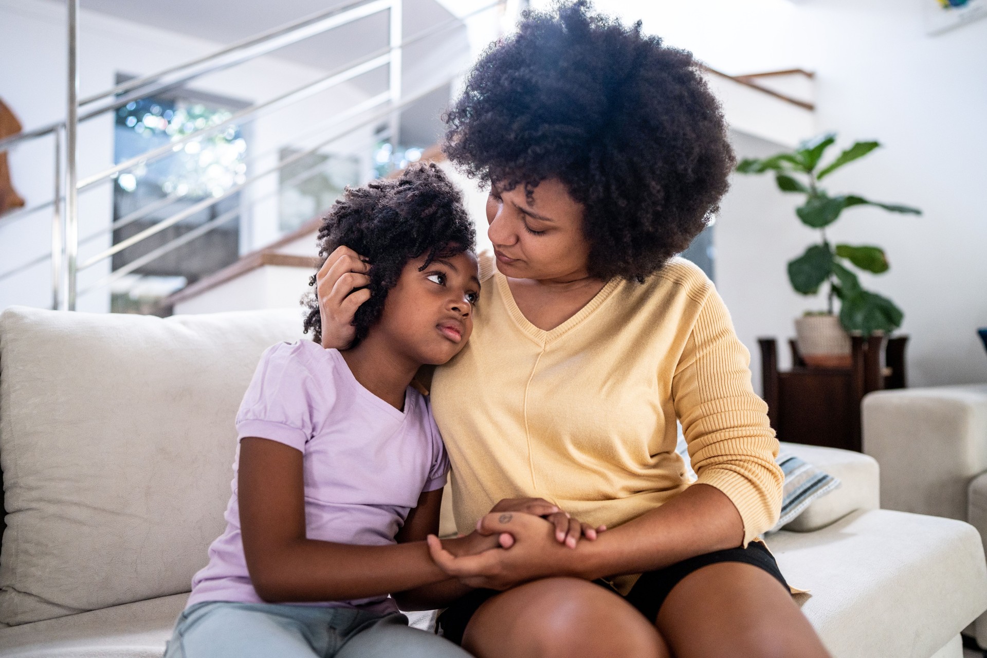 Mother embracing her sad daughter on sofa in the living room